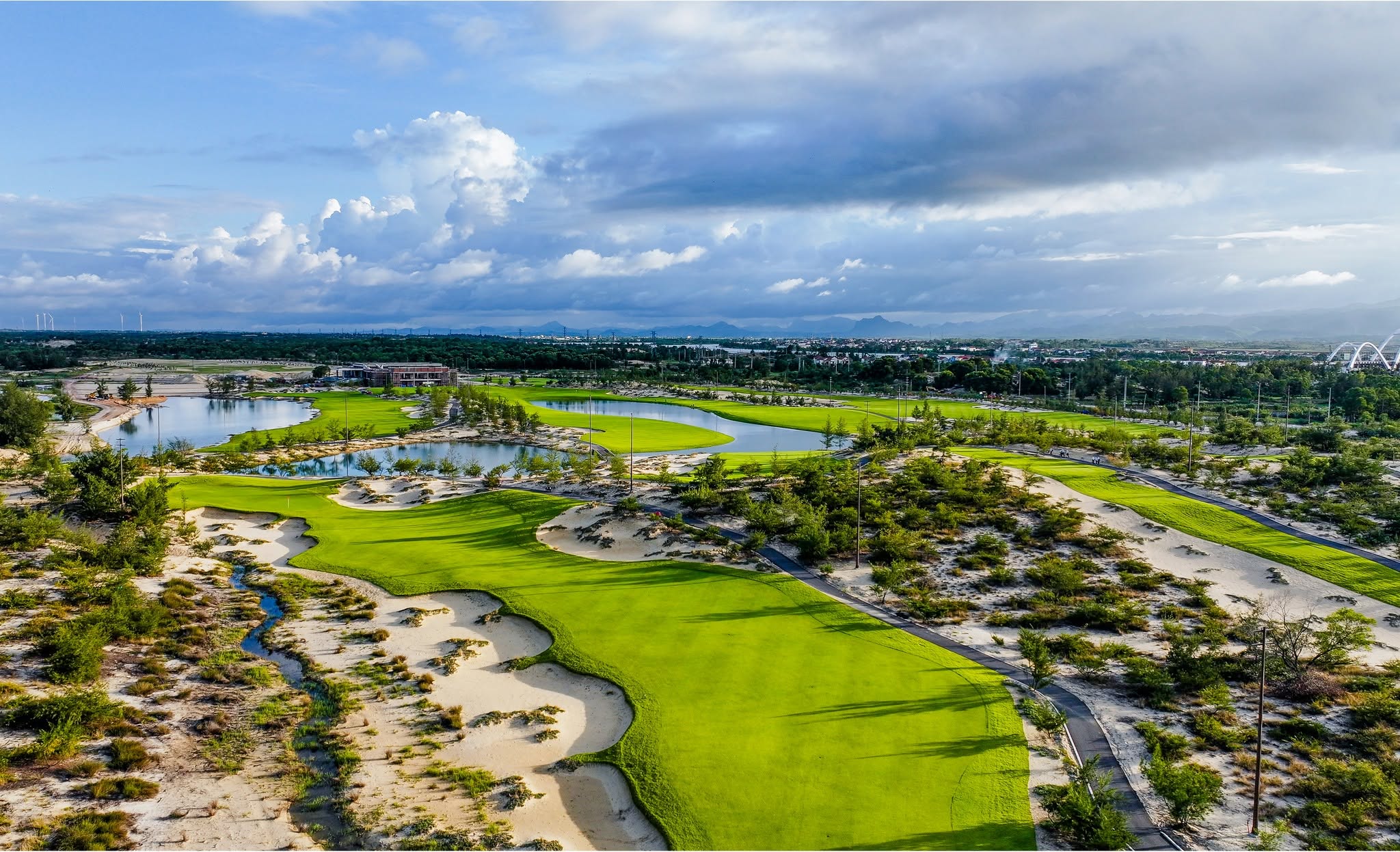 Blue Diamond Golf Links is situated on the Bao Ninh Peninsula in Dong Hoi Ward, Quang Tri Province, offering golfers a distinctive coastal golfing experience with a classic links-style design. The course embraces the natural beauty of the seaside landscape, featuring rolling sand dunes, wide-open spaces, and panoramic ocean views. Exposed to coastal winds and built on firm, sandy terrain, the course allows for longer ball rolls while demanding greater precision and control from players. Deep bunkers, uneven terrain, and constantly changing wind conditions add complexity to each round. The natural sea breeze can significantly influence ball direction and distance, making club selection and shot execution essential to navigating the course successfully. Blue Diamond Golf Links